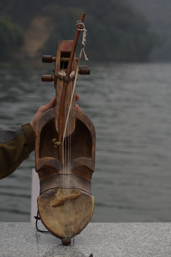A handmade Nepali sarangi held by a person at a serene lakeside, showcasing local craftsmanship.