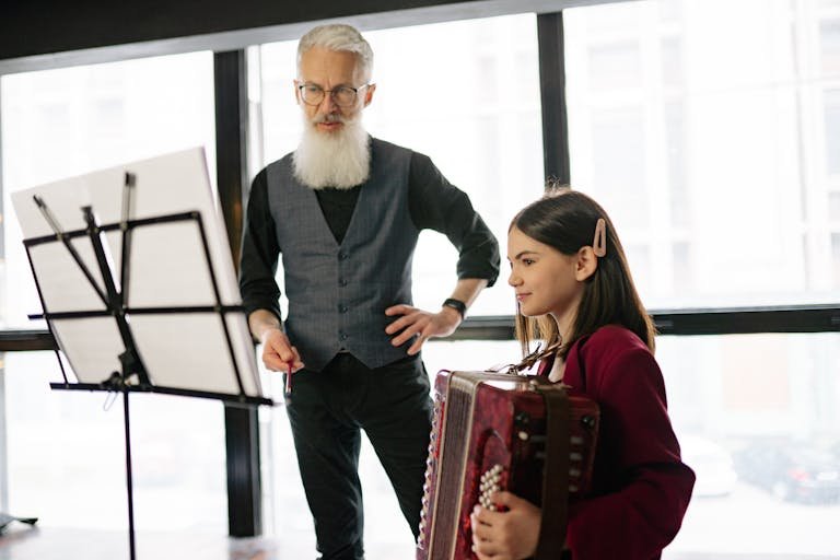 A teacher instructing a young girl playing the accordion during a music lesson indoors.
