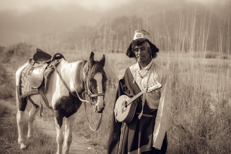 A traditional Nepalese musician with a string instrument standing beside a horse in a rural landscape.
