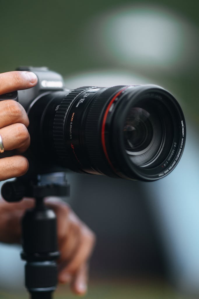 Detailed close-up of a DSLR camera with lens on a tripod held by a person.