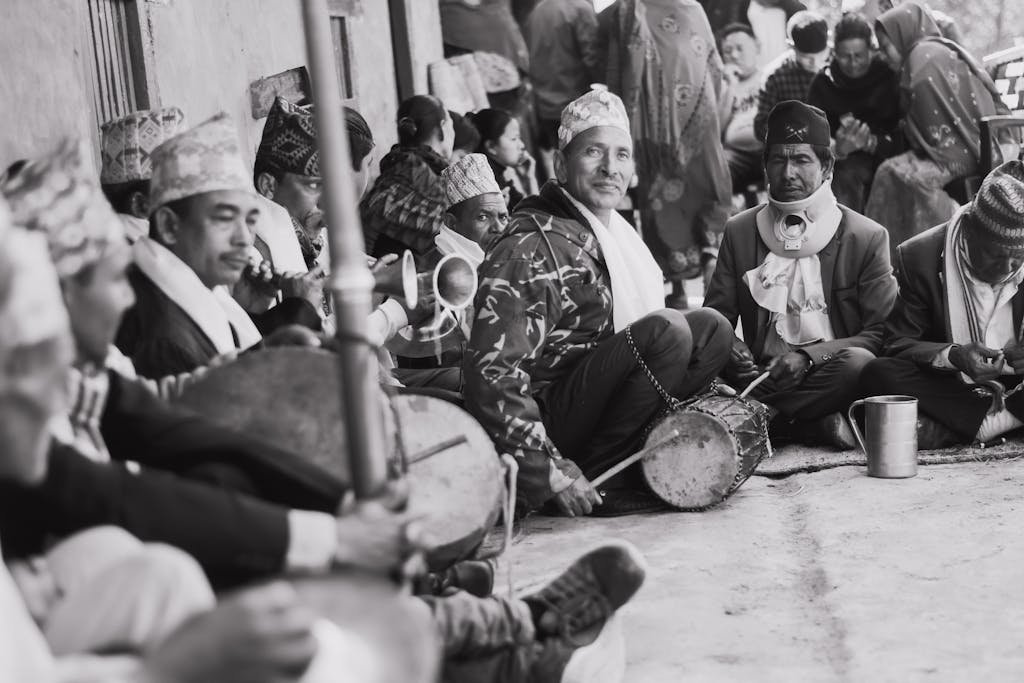 A group of traditional Nepali musicians playing instruments in a cultural setting. Black and white capture.